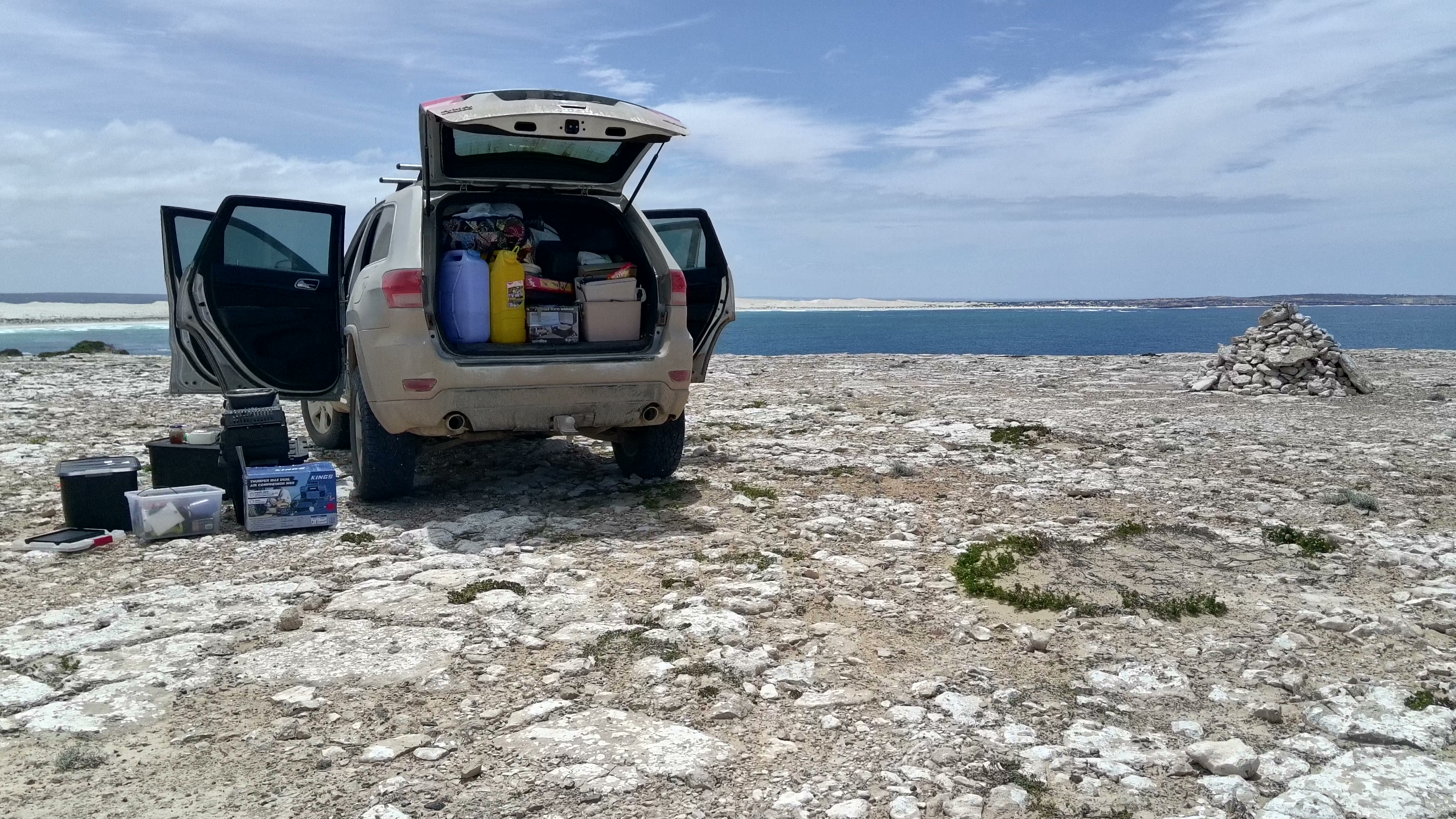 Expedition Jeep Grand Cherokee parked with tailgate open by the stone cairn overlooking the cliffs.